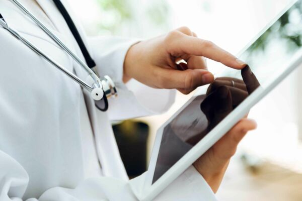 Das Titelbild zeigt die Hand eines Arztes, die gerade etwas auf einem Tablet-PC eintippt.