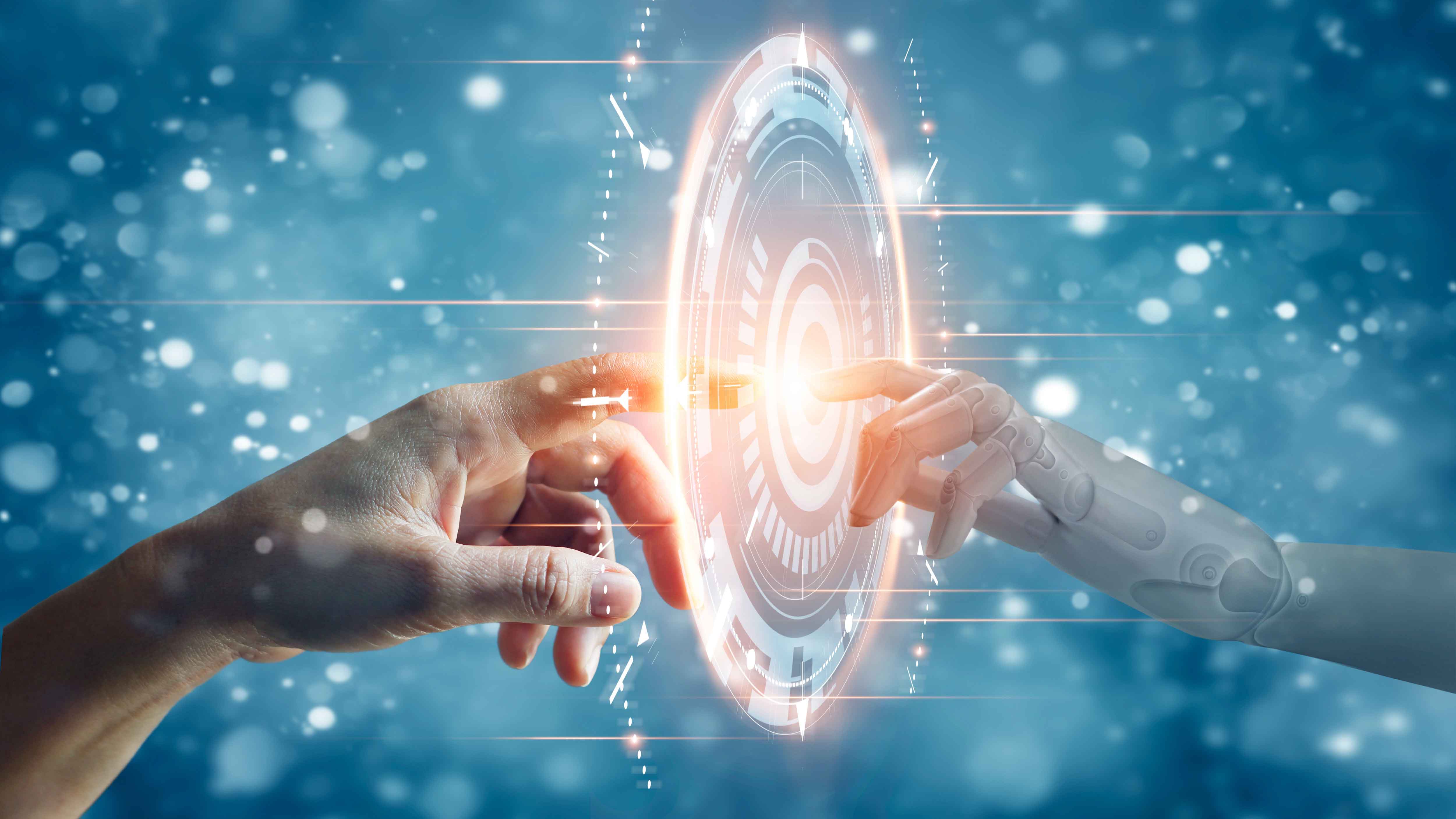 Das Symbolbild zeigt eine menschliche Hand und eine Roboterhand in einem virtuellen Raum, deren Zeigefingerkuppen sich berühren. Um die Stelle herum, an der sich die Fingerkuppen berühren, ist ein leuchtendes, rundes virtuelles Gebilde zu sehen, das einer