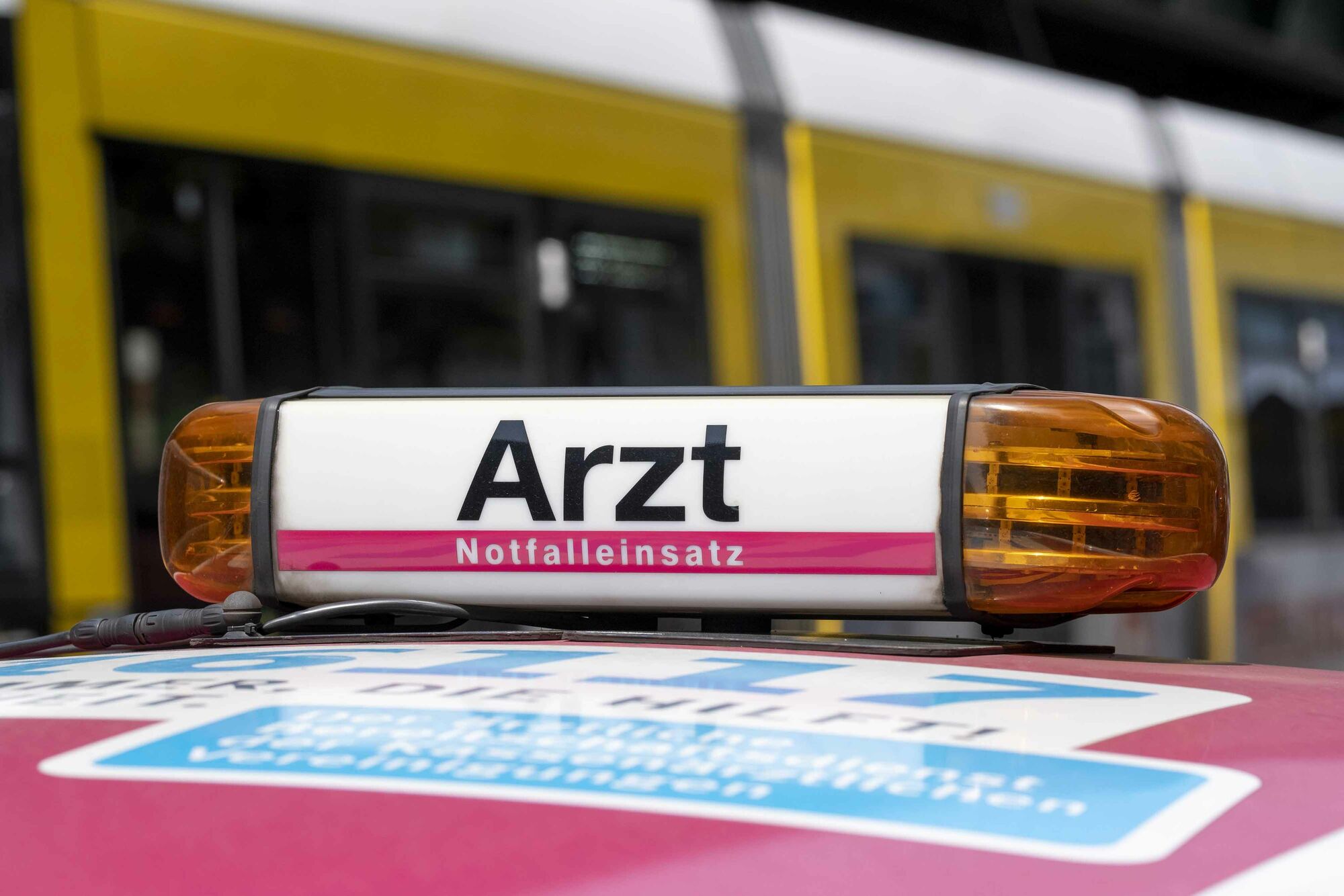Das Foto zeigt das Signallicht auf dem Dach eines 116177-Einsatzfahrzeugs. Auf dem Signallicht steht „Arzt – Notfalleinsatz“. Im Hintergrund ist in der Unschärfe eine Straßenbahn zu sehen.