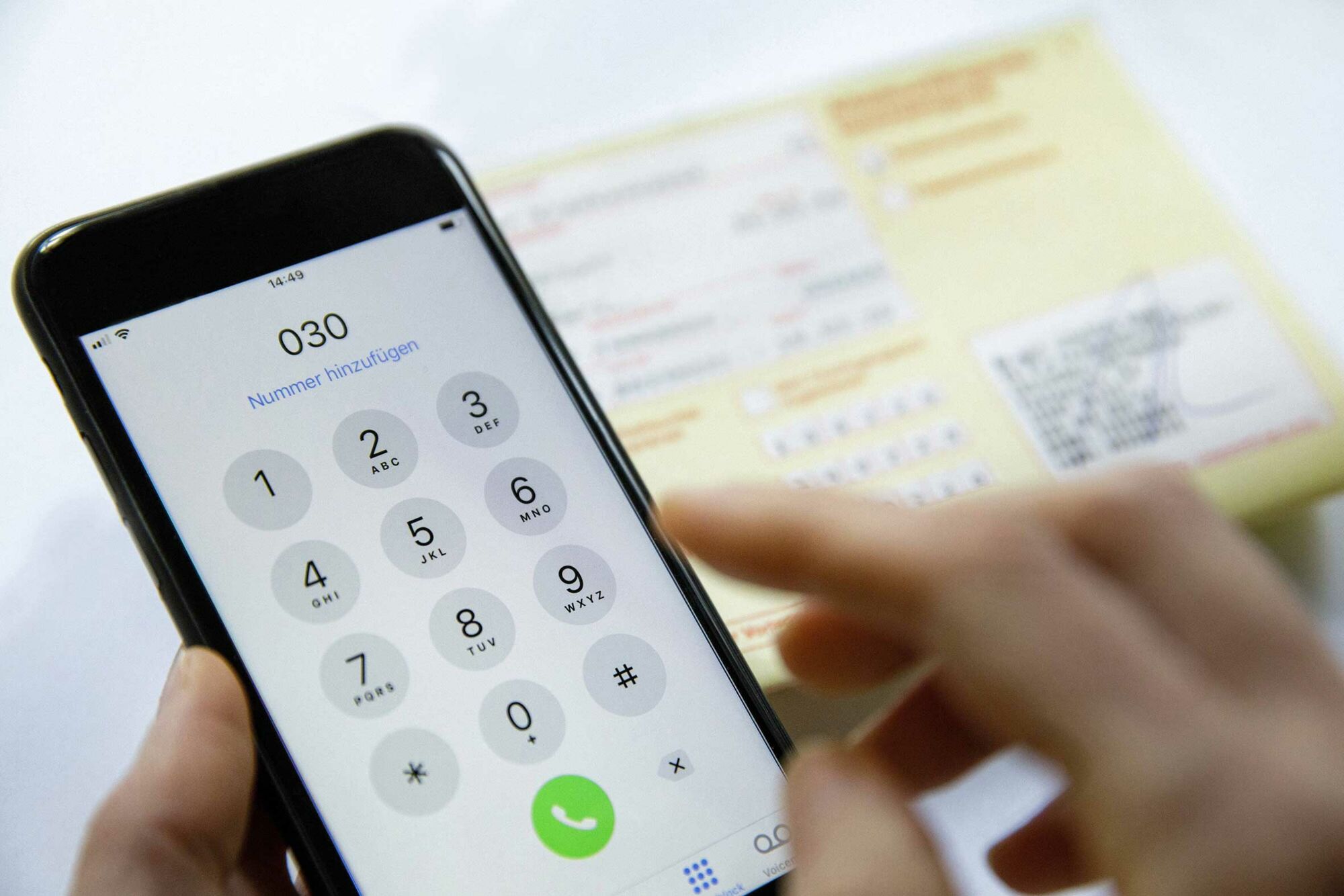 Das Foto zeigt Hände, die eine Nummer in ein Mobiltelefon tippen. Im Hintergrund liegt eine Arbeitsunfähigkeitsbescheiniung.