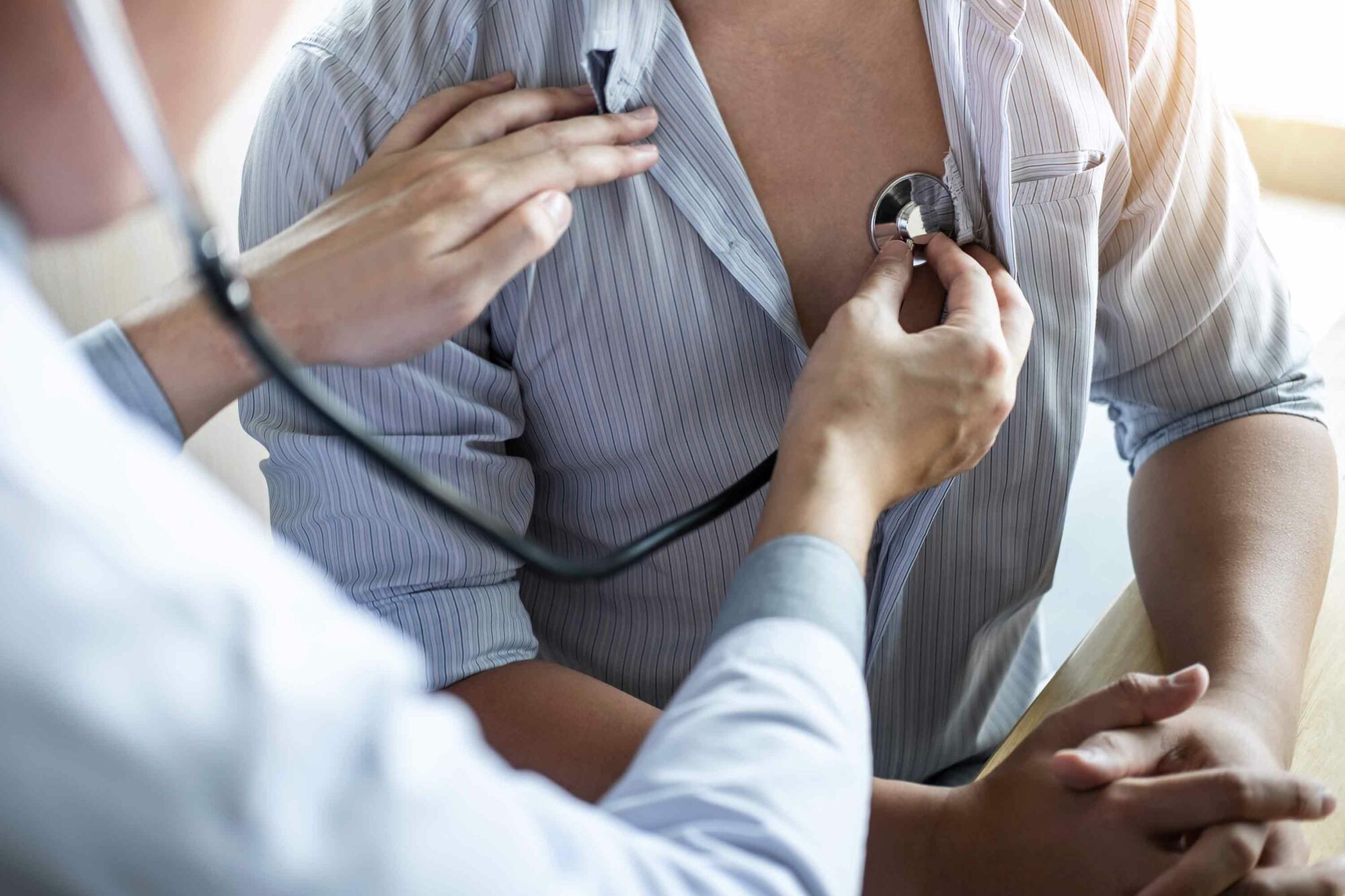 Das Foto zeigt einen Arzt, der mit einem Stethoskop das Herz eine Patienten abhört.